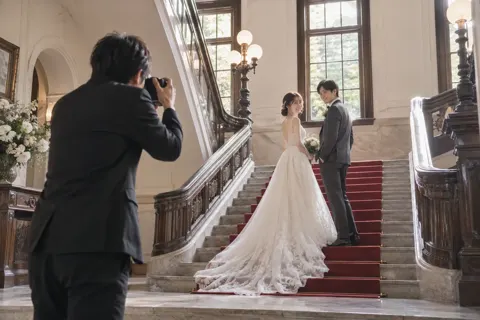 洋館の階段でドレスの2人を撮るカメラマン（フォトウェディング・前撮りの写真 No.19）