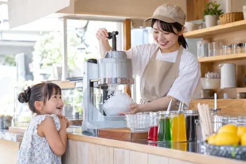 氷削機で氷を削る店員と、それをながめる子ども（アイス・クレープ・かき氷の写真 No.21）