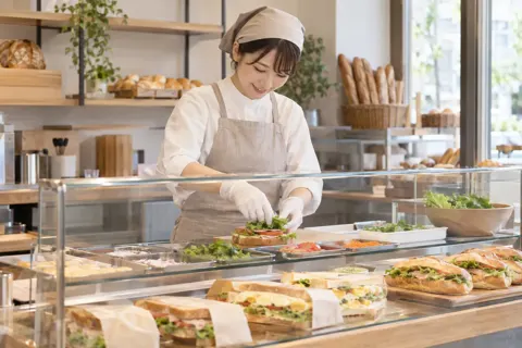 ショーケースでサンドイッチを作る店員（パン・ベーカリーの写真 No.33）