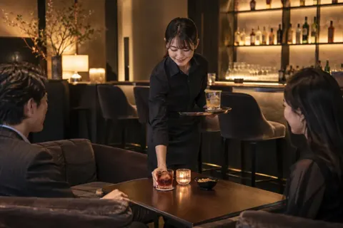 バーのソファ席にグラスを運ぶスタッフ（バー・ショットバーの写真 No.33）