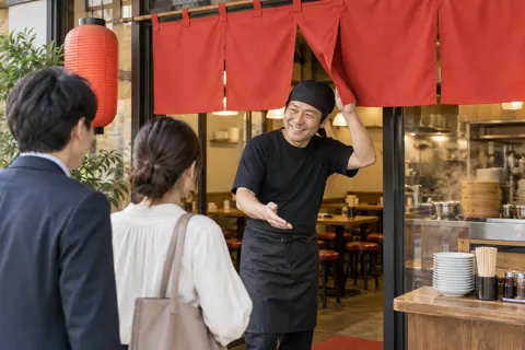 赤いのれんの中華料理店に入るお客様と迎える店員（中華・餃子の写真 No.24）