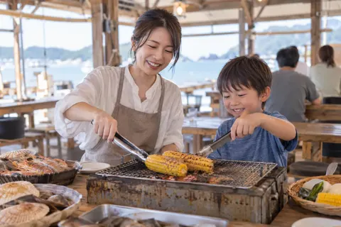 子どもと一緒に網でとうもろこしを焼く親（浜焼きの写真 No.19）