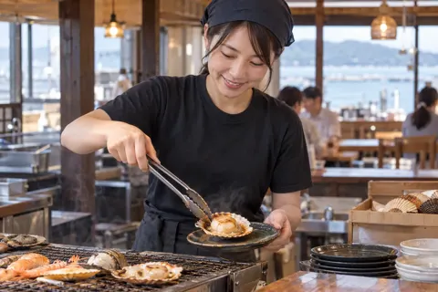焼けたほたてを皿にのせる店員（海鮮丼・浜焼きの写真 No.23）