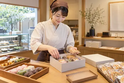 和菓子とせんべいの詰め合わせを箱に入れる店員（和菓子・団子・せんべいの写真 No.19）
