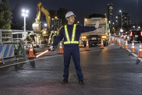 夜の道路工事で光るベストを着て立つ警備員（警備・セキュリティの写真 No.27）