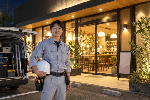夜に明かりがついた店舗と作業を終えた電気工事士（電気工事・空調・電気設備の写真 No.47）
