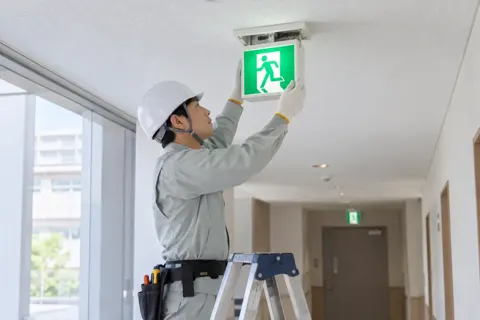 非常口の誘導灯を取りかえる作業員（電気工事・空調・電気設備の写真 No.52）