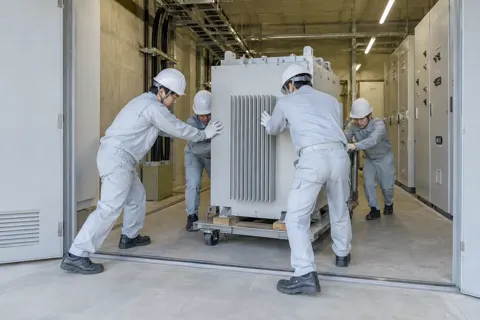 電気室に大きな機械を運び入れる作業員たち（総合建設・ビル・マンション・店舗・工場の写真 No.62）