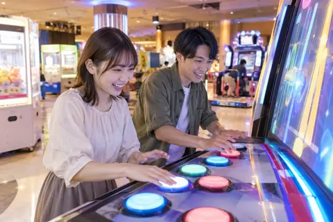 リズムに合わせてボタンを押すゲームで遊ぶ二人（ゲームセンター・ボウリング・ビリヤードの写真 No.23）