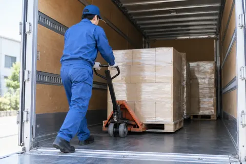 パレットの荷物をハンドリフトで荷台の奥へ運ぶドライバー（運送・配送・トラックの写真 No.60）