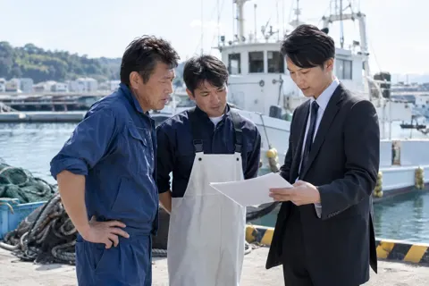 作業着の船員たちと書類を見る海事代理士（海事代理士の写真 No.23）