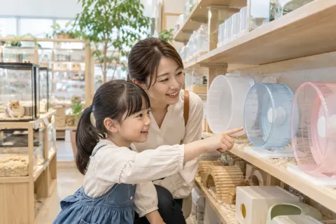ハムスターの回し車を選ぶ子どもと親（ペット用品店の写真 No.25）