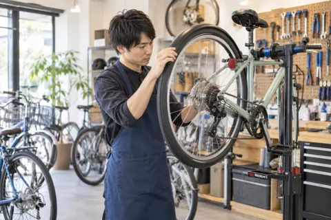 スタンドにかけた自転車の車輪を回して確かめる店員（自転車販売・修理の写真 No.32）