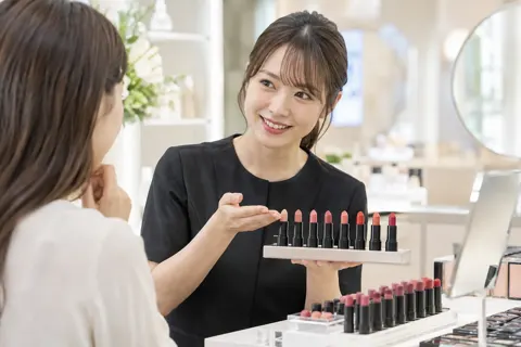 口紅の色を何本もならべて見せる店員（コスメ・化粧品の写真 No.27）