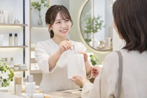 見本の小さなびんをふくろに入れてわたす店員（コスメ・化粧品の写真 No.41）