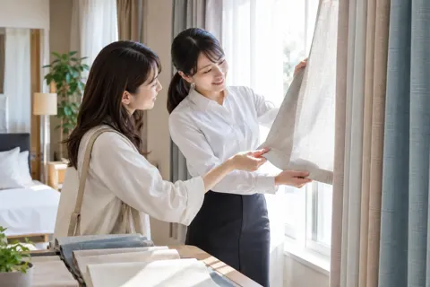 カーテンの布の見本を窓に当てて見るお客様と店員（寝具・カーテンの写真 No.20）