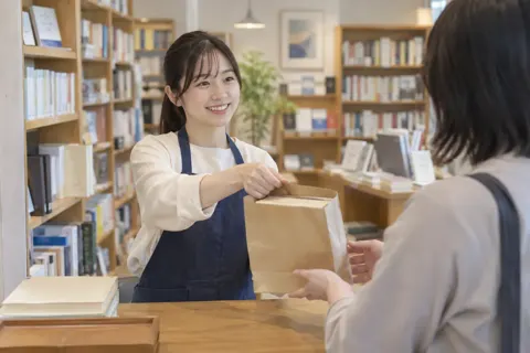本をふくろに入れてわたす店員（書店・古書の写真 No.20）