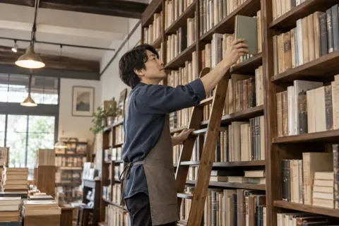 古書の棚からはしごで本を取る店主（書店・古書の写真 No.31）