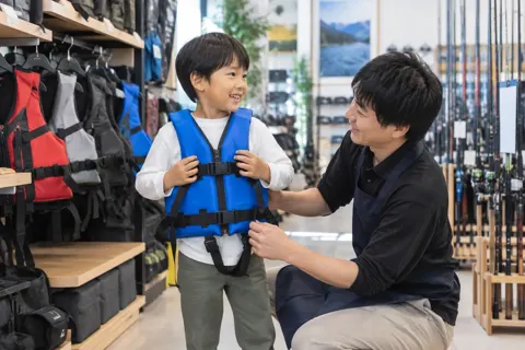 ライフジャケットを着てみる子どもと店員（釣具店・フィッシング用品の写真 No.25）