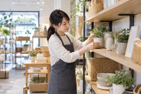 棚の品物のならべ方をかえる店員（雑貨・インテリア小物の写真 No.28）