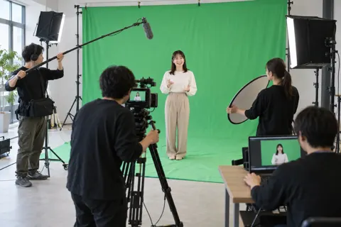 緑色の布の前に立つ出演者と撮影チーム（映像制作の写真 No.22）